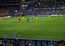 Chelsea (blue) and Barcelona players (yellow) leave the pitch at the end of the first half of their semi-final second leg at Stamford Bridge. The referee is talking to two Barcelona players.