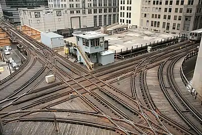 Chicago Transit Authority control tower 18 at this three-quarter union guides elevated Chicago 'L' north and southbound Purple and Brown lines intersecting with east and westbound Pink and Green lines and the looping Orange line above the Wells and Lake street intersection in the Loop.