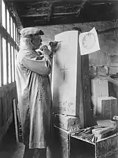 a man carving the a maple leaf onto a gravestone, in a workshop, with a hammer and chisel.