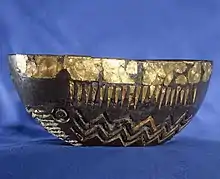 an oval bowl, made of shale, tin and embossed gold, represents a sea-going boat with circular shields, oars and waves represented in its design.