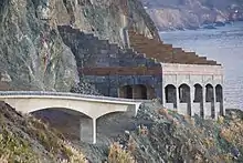 A highway bridge leads to a rock shelter protecting the roadway from rocks falling off the cliff above.