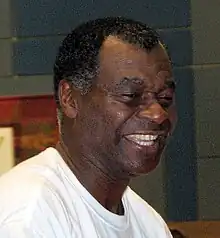 A black person, wearing white t-shirt, is smiling and looking to the right.