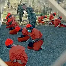 Kneeling prisoners at the Guantanamo Bay detention camp with eyes and ears covered