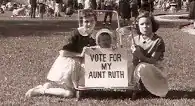 Photo of two woman seated holding a sign saying "Vote for My Aunt Ruth