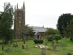 Stone building with square tower. In the foreground are gravestones and trees.