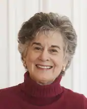 color headshot of an older white woman with short hair wearing a maroon turtleneck sweater