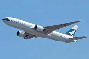 Front quarter view of the first 777 built in flight wearing Cathay Pacific livery and with flaps partially extended and landing gear retracted.