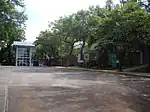 Asphalted courtyard with a garden with several trees and surrounded by a building with several glass windows