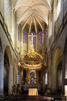 Photographie d'un chœur d'église avec des murs en pierre beige surmontés de voûtes en pierre blanche