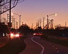 Street lamps lit, car headlights on, electricity infrastructure silhouetted in distance