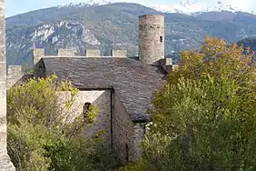 Stone building with slate roof. A tower protrudes from the right end of the roof.