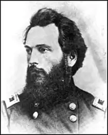 Black and white photo shows a bearded and dark-haired man in a dark uniform with two rows of buttons.