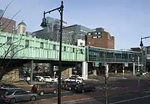 An elevated railway station in an urban area. The left half is patinaed copper; the right half curved glass.