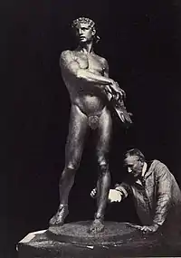 A black and white photograph of a sculpture of a man, with the sculptor behind it