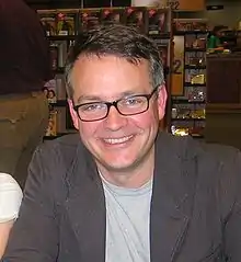 a smiling man wearing glasses faces the camera