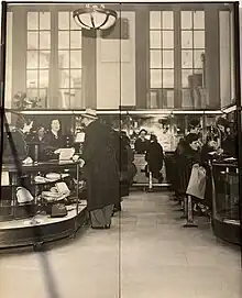 Black and white photo of women in black on both sides of a long counter looking at jewelry