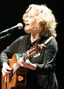 Chava Alberstein playing guitar and singing into microphone onstage