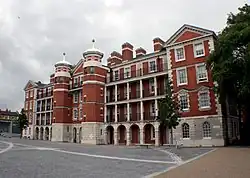 A four-story building of light grey stone and red brick with a complex facade including two central towers, and pillar and arch verandahs on the face of three of the four storeys