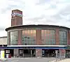 A brown-bricked building with a light blue strip over the doorway containing a darker blue sign reading "CHISWICK PARK STATION" in white letters