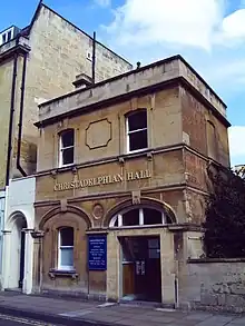 Rectangular yellow stone building with flat roof and arched doorway.