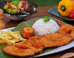 Image 25Cutlet "Valluna", a typical dish of the Valle del Cauca region of Colombia and the Afro-Colombian culture of the area near the Pacífic Ocean. It includes a milanesa, usually prepared with a lean pork loin beef or chicken can also be used. Traditional accompaniments include rice, sliced tomatoes, onions, chopped fried plantains or fries and a drink called "Lulada" made with lulo fruit, water and sugar (from Culture of Colombia)