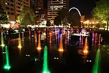 In this low aerial night shot, numerous fountains shoot water into the air, illuminated by colored lights.