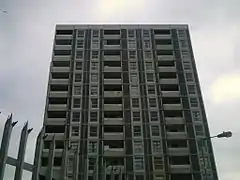 Eleven storeys of a gray residential tower, with a spiked fence and a lamp in the foreground.