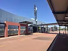 Concrete station entrance building with bus road in front and shelters on either side of the road