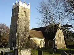 A stone church seen from the southwest. Nearest is the tower with a battlemented parapet bearing statues, then a short nave, and a larger south transept