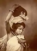 A Kochh Mandai woman of east Bengal (present-day Bangladesh) shown with a broad-bladed agricultural knife and carrying a freshly harvested jackfruit. (1860)