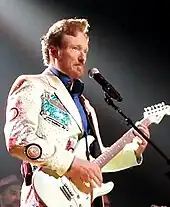 Conan O'Brien playing the guitar in a white suit