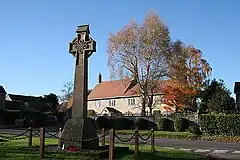 Celtic pattern stone cross in the foreground with trees and houses in the background.