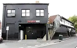 A black two-story building on a sidewalk