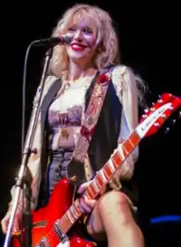 Woman playing guitar, with her left leg up on a monitor.