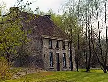 Photo of a two-storey brick house on the left partially obscured by trees with a front lawn and with a row of trees on the right