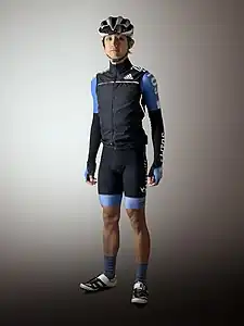 Typical spring/autumn cycling attire comprises the summer kit with an additional insulated vest and arm warmers. Also worn is a pair of sunglasses resting on the helmet vents.