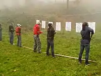 A line of people in front of targets reaching for their guns in holsters.