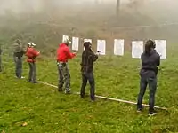 A line of people in front of targets drawing guns from holsters.