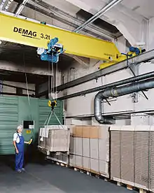 Circa 2010 Demag Overhead crane and hoist (device) being used in typical machine shop. The hoist is operated via a wired pushbutton station, known as a pendant, to move the system and the load in any direction