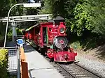 A red steam locomotive with a 2-4-0 wheel arrangement and its tender