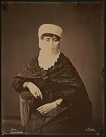 Sepia-toned portrait of a woman seated on a chair, wearing traditional Turkish clothing, including a veil