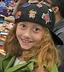 Head and shoulders of Fischer, an eight-year old girl with reddish blonde hair in a black baseball cap and green costume