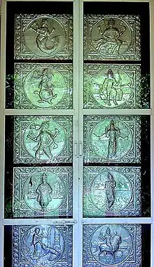 A silver door with ten panels in two columns. The panels depict from top left clockwise a lion-faced man, a man with a bow and axe, a man with a bow, a man playing a flute, a man on a horse, a man with one of his feet on the head of a kneeling man, an arms-akimbo man, a boar-faced man, a man whose body below the waist is a tortoise and a man whose body below the waist is a fish.