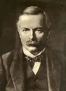 A middle-aged man with a large moustache looks into the camera