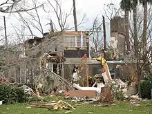 What was a brick two-story home has had its roof and parts of the second floor torn off. Debris and tree branches are strewn all over the surrounding lawn.