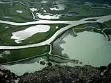 A large number of irregularly shaped bodies of water separated by stretches of green vegetation and bordered by grey rocks at the bottom.