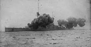 A large warship is partially obscured by smoke from its main guns firing.