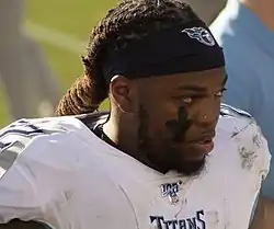 Derrick Henry wearing his Titans football uniform, but no helmet, on the sidelines.