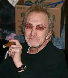 Photograph of Dewey Martin sitting in a chair and smoking a cigar