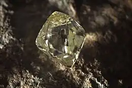 A clear octahedral stone protrudes from a black rock.